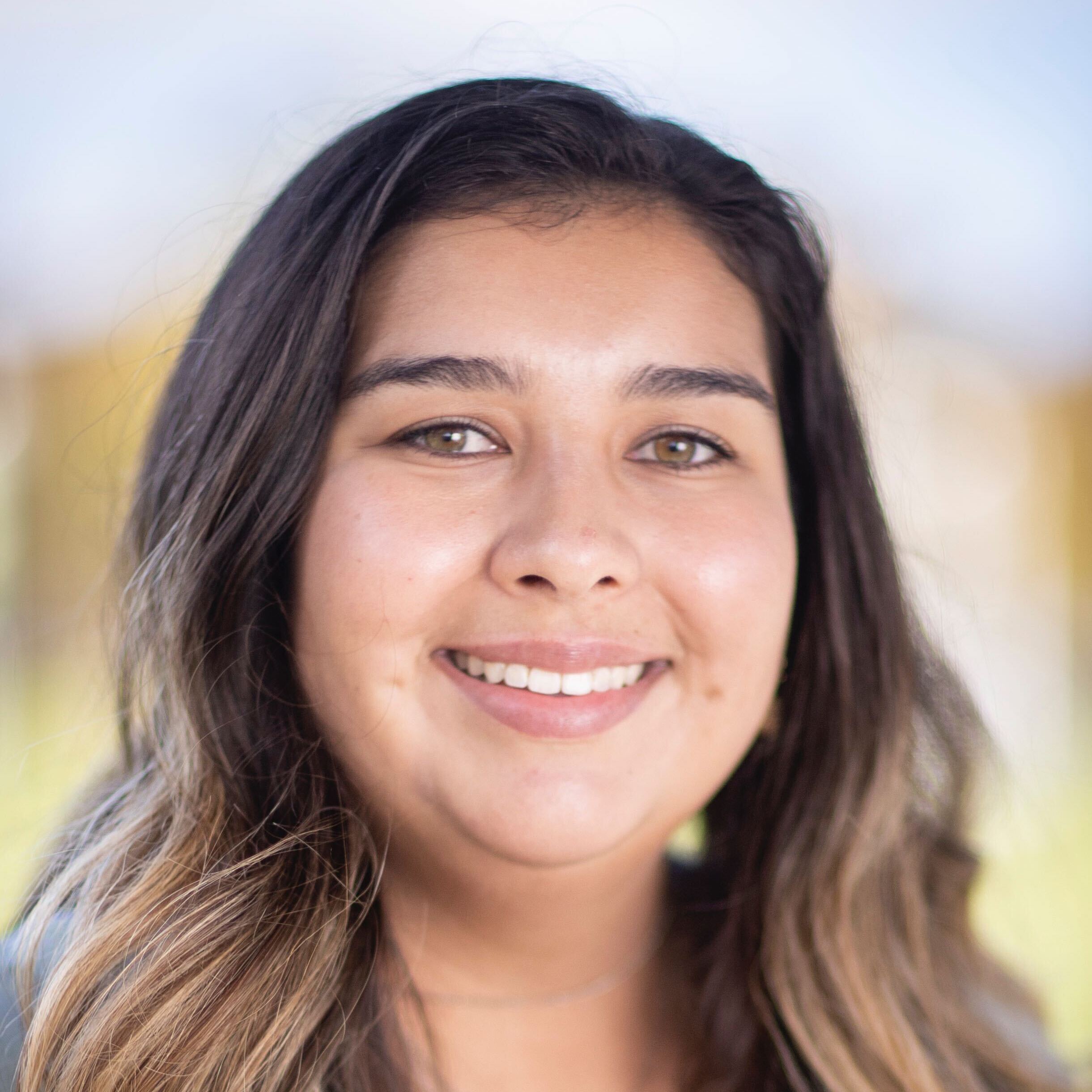A headshot of a smiling woman with long brown hair and hazel eyes