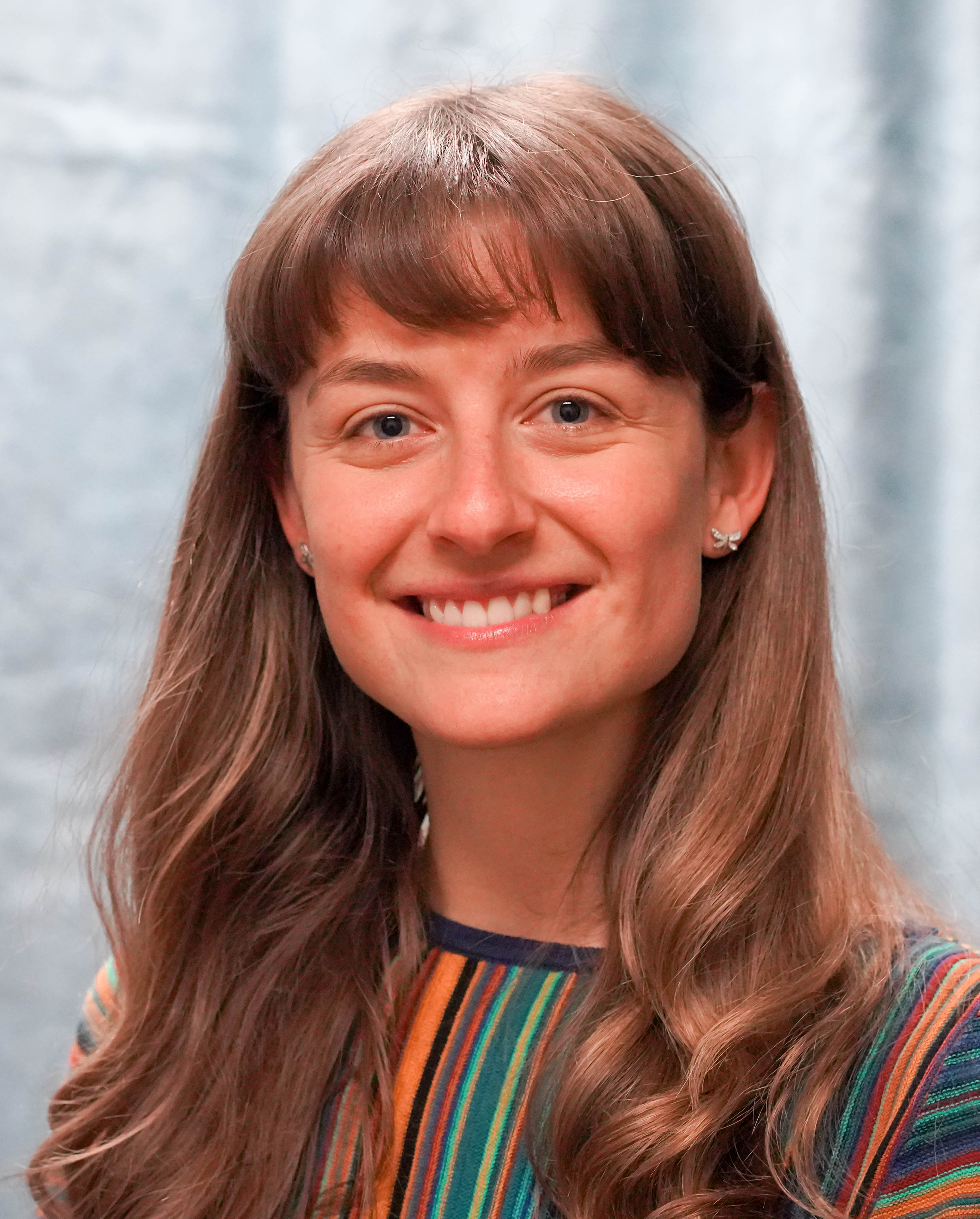 A headshot of a smiling woman with long light-brown hair and blue eyes
